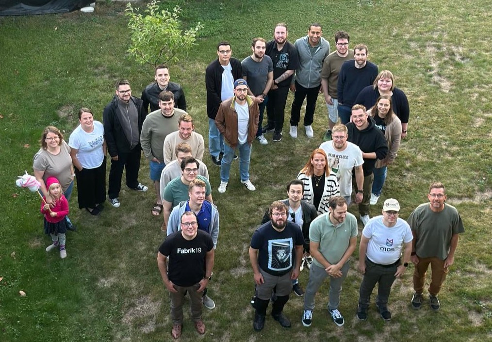 Fabrik19-Team steht zusammen auf einer Wiese in der Form der Zahl 12